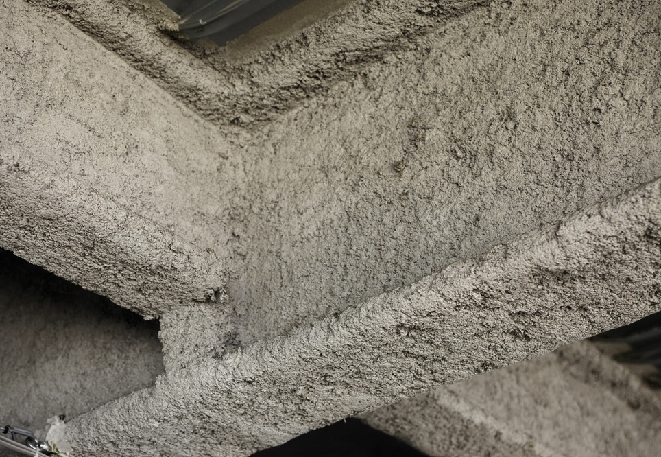 鉄骨の梁に厚く吹き付けられた、灰色で表面が凹凸としているアスベスト含有吹き付け材のクローズアップ