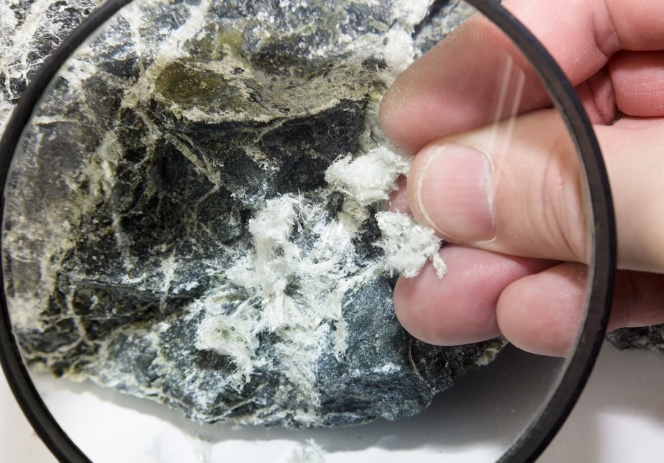 白い綿状のアスベスト繊維を、ルーペで拡大して見ている様子。指で繊維の質感を確かめている