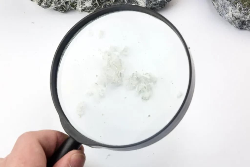 拡大鏡で石中のアスベスト繊維を調べる手