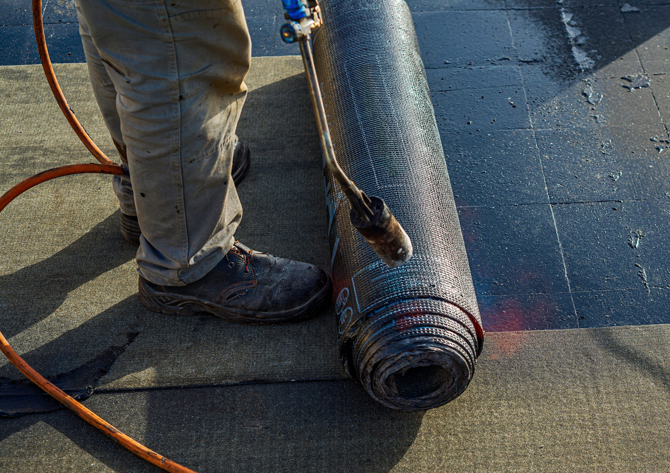 専用のバーナーでアスファルト防水シートを熱している男性の足元