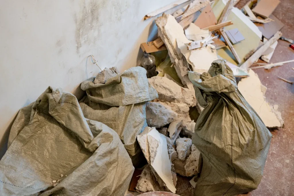 細かく砕かれたコンクリートや漆喰が詰まった数袋の重い袋が、うず高く積まれた瓦礫の山の横に置かれています