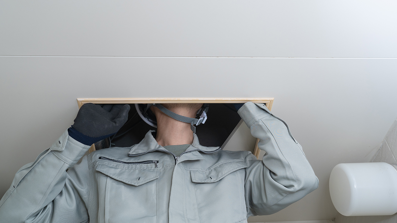 アスベスト調査でユニットバスの天井裏を確認する作業員