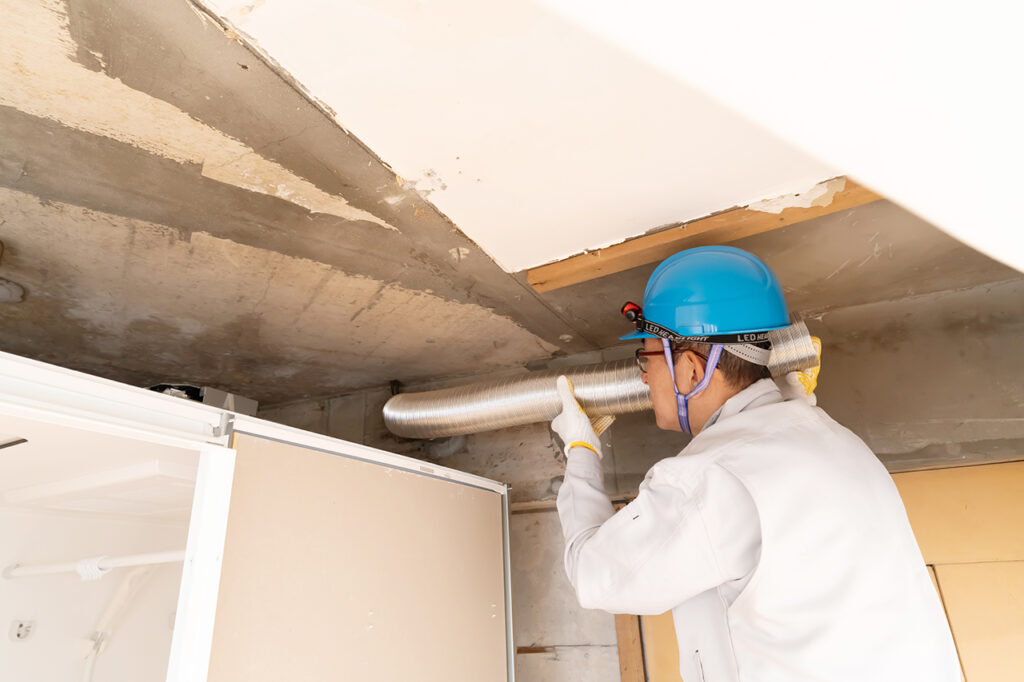 壁から出る配管を調査する作業員