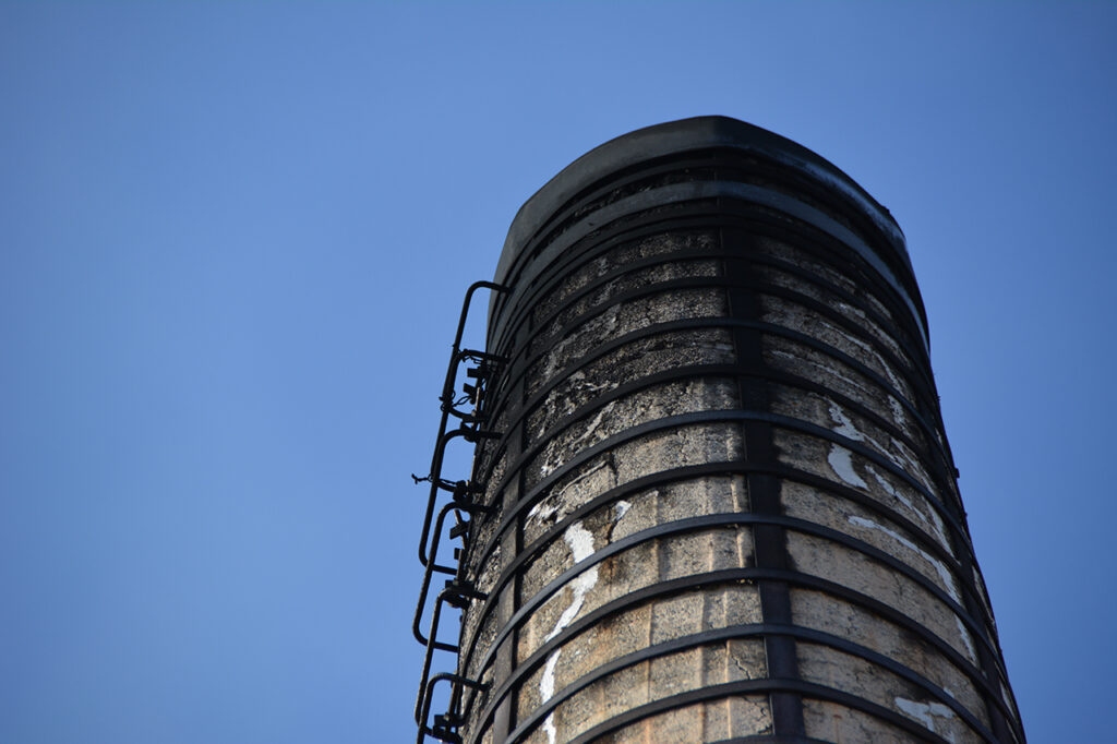 補強用の鉄バンドが巻かれた古いコンクリート製の煙突を下から見上げている