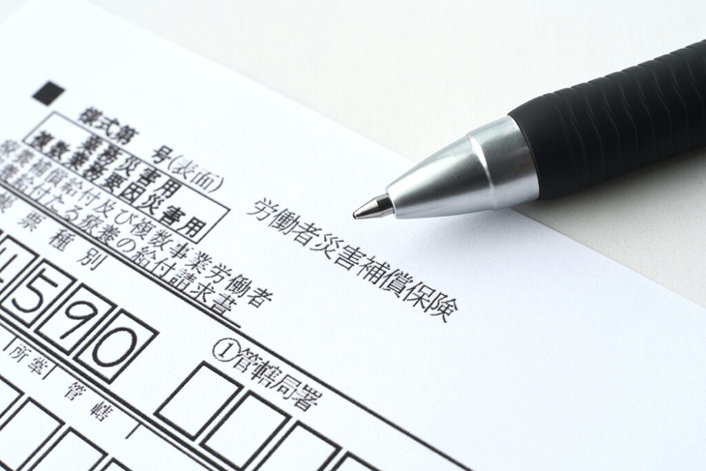 書類の上に置かれた黒いボールペン。書類のタイトルは『労働者災害補償保険』と書かれている。