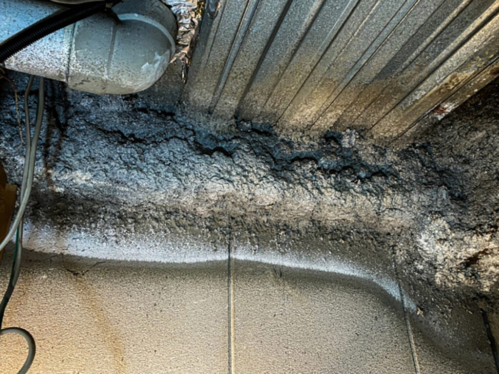 建物の天井裏にある金属デッキプレートと梁の表面に、グレーの吹付け材が施工されている