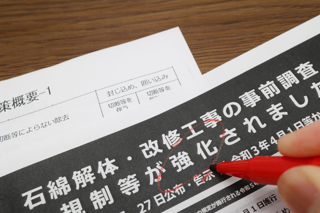 「石綿解体・改修工事の事前調査 規制等が強化されました」と印字された法改正の案内文書に、赤いペンで下線を引き確認している